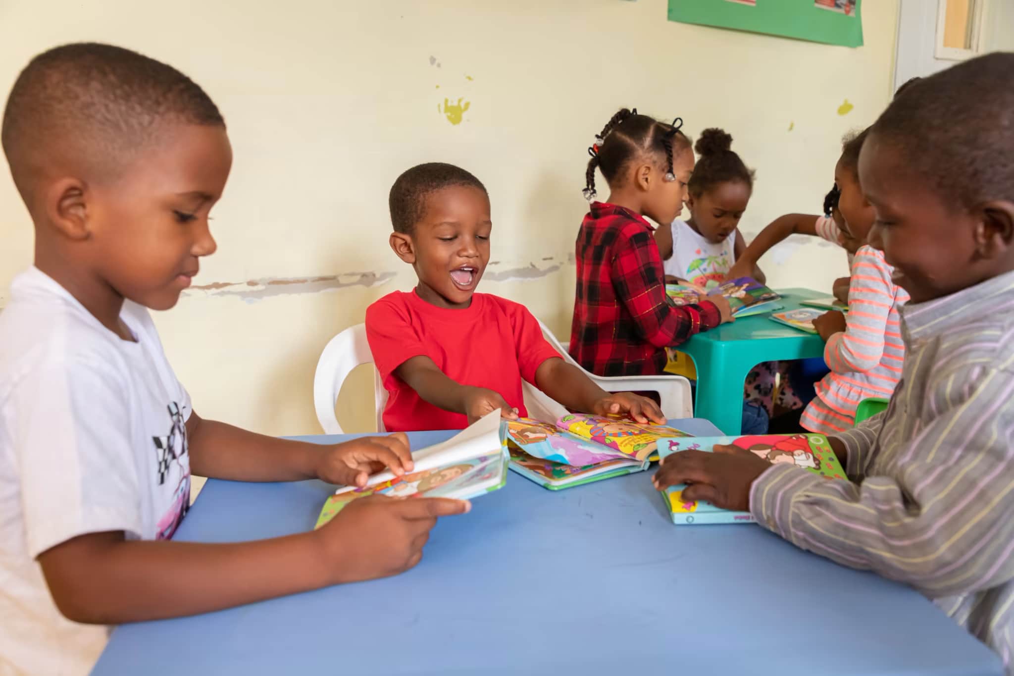 Kinderpatenschaft - Eine Gruppe von Kindern sitzt um einen Tisch herum, liest und lächelt.