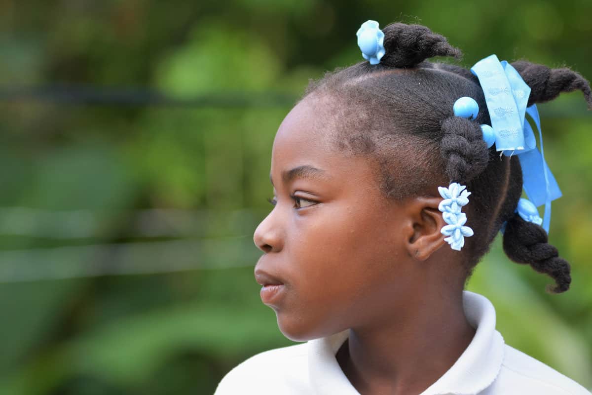 Haiti: una bambina guarda di lato. Ha dei fiocchi blu tra i capelli intrecciati.
