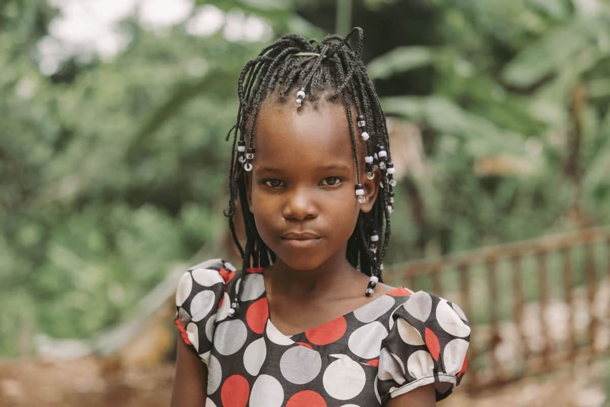 Haiti: una bambina indossa un abito a fantasia e i suoi capelli sono intrecciati con perline bianche.