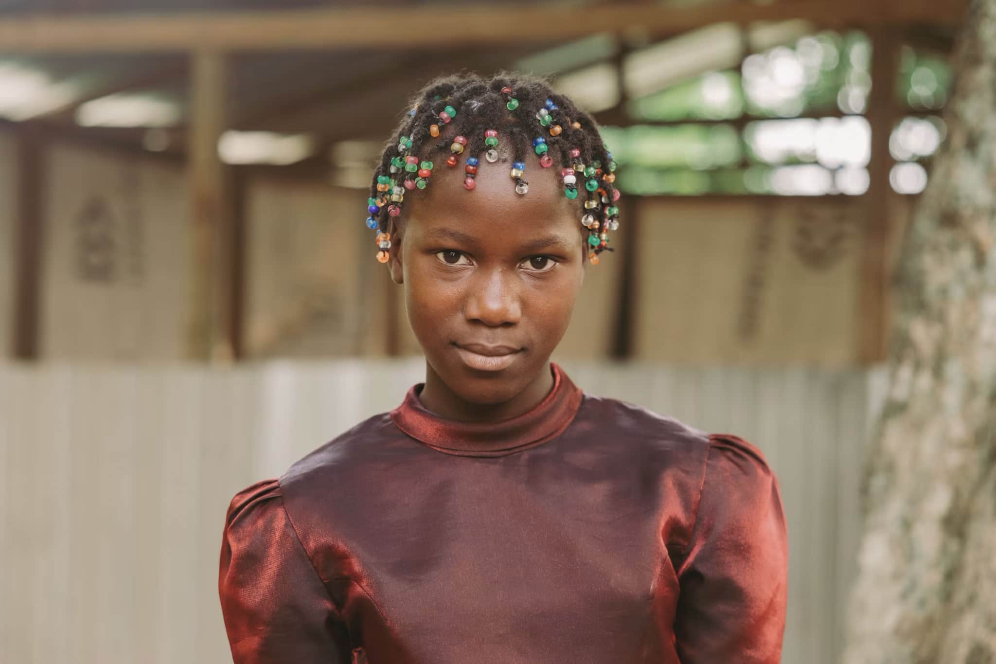 Haiti: una ragazzina con un vestito rosso guarda la macchina fotografica. I suoi capelli sono intrecciati con perle.